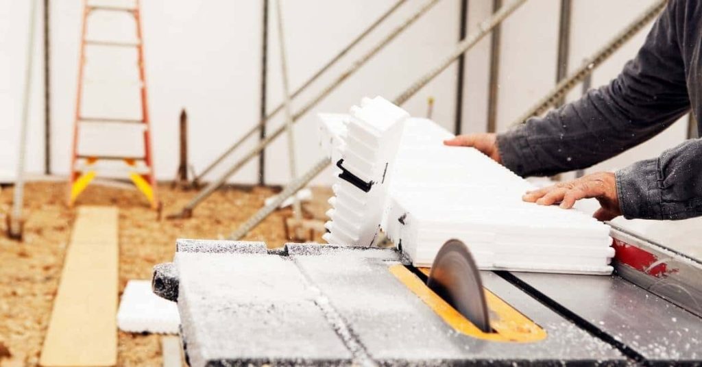 Person cutting white foam insulation board on table saw