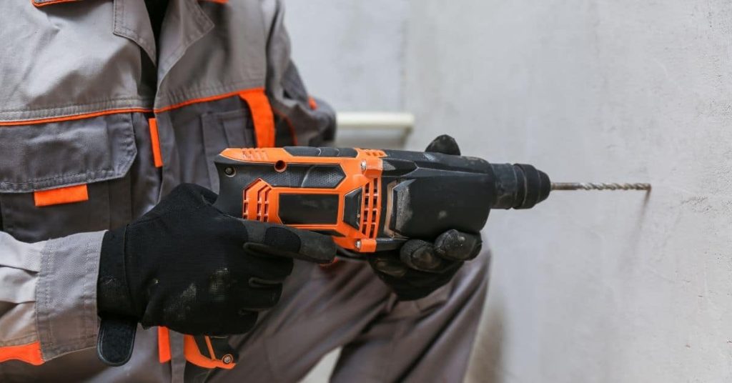Person drilling concrete wall with orange and black cordless drill