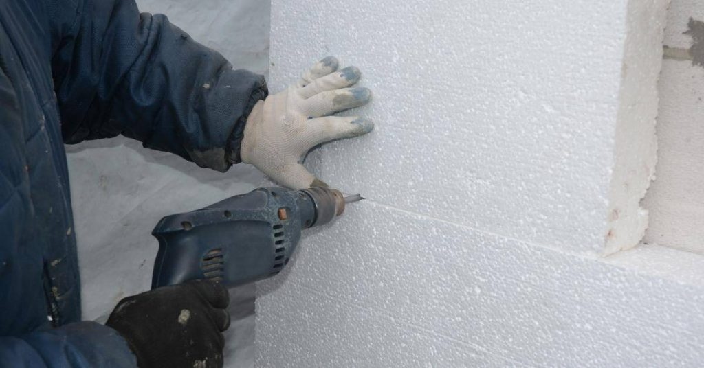 Person drilling into foam insulation board on block wall