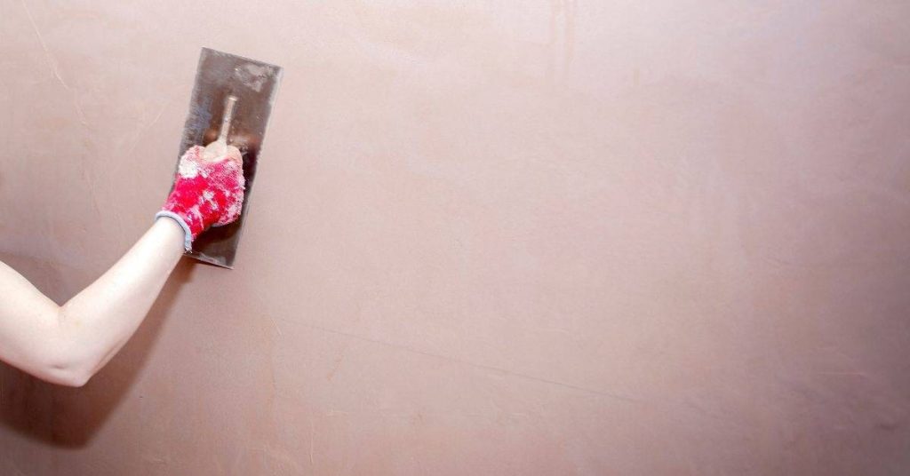 Person smoothing plaster on wall with trowel wearing red glove