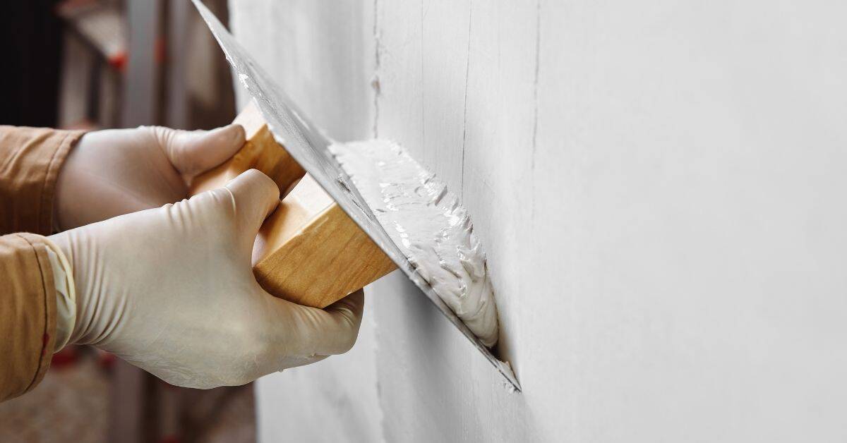 Hands wearing gloves applying plaster to wall with trowel