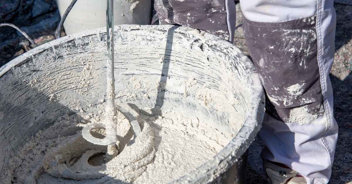 close up of person mixing plaster in bucket with drill mixer