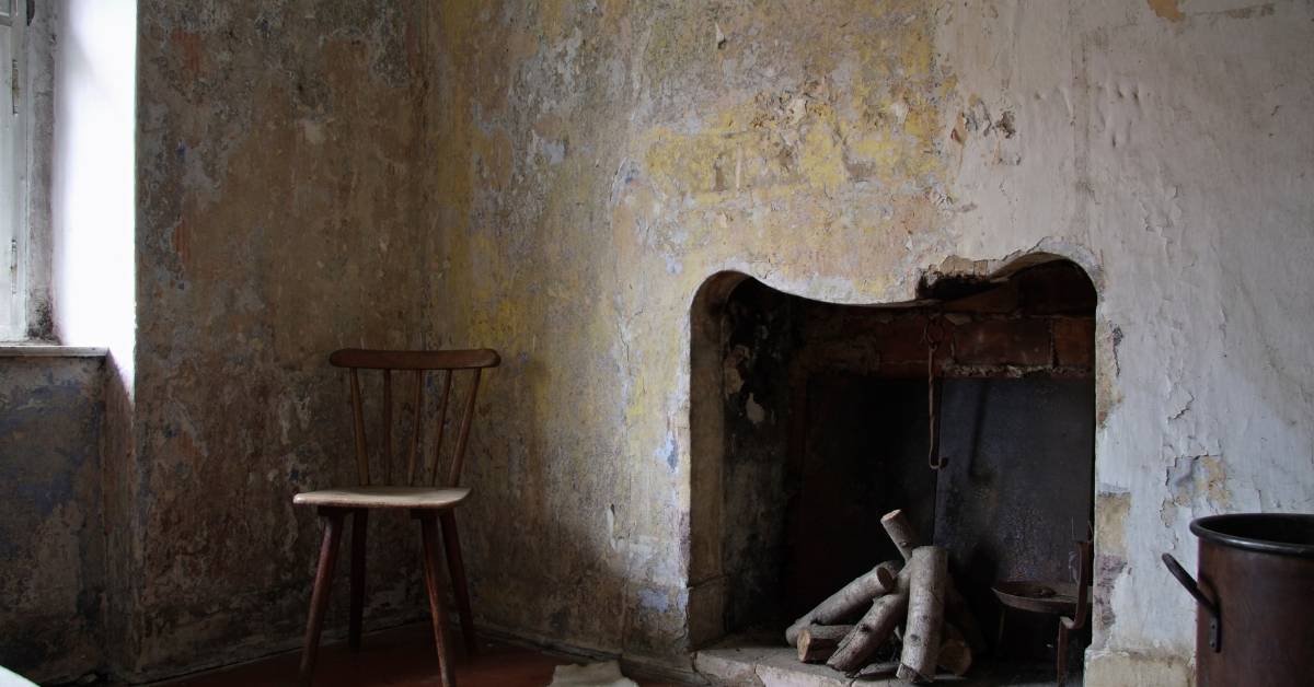 Old plaster wall with peeling paint and a fireplace with logs