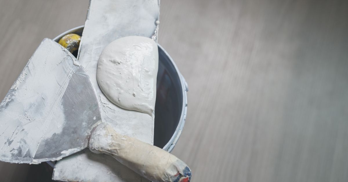 metal plastering trowel and hawk with wet plaster over bucket