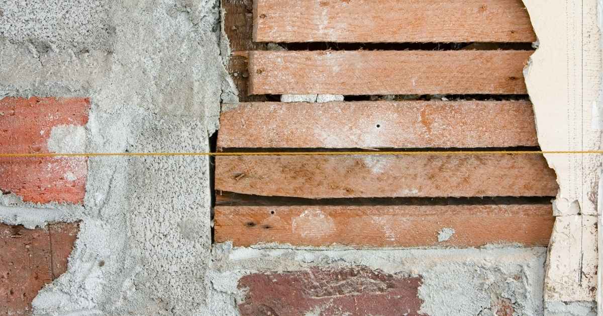 Exposed wooden lath behind broken plaster with string line