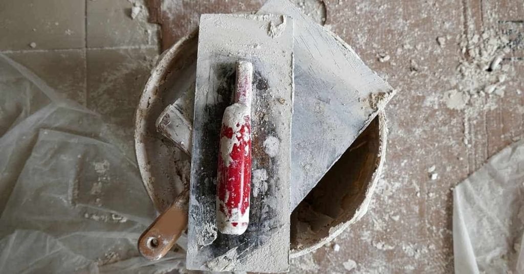 Plastering trowel with red handle on bucket filled with plaster