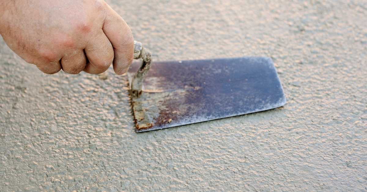 Hand using metal trowel on rough stucco surface