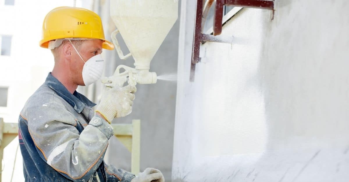 Construction worker spraying stucco onto exterior wall