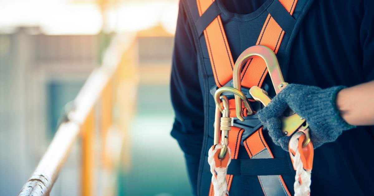 Close up of worker wearing orange safety harness with carabiners