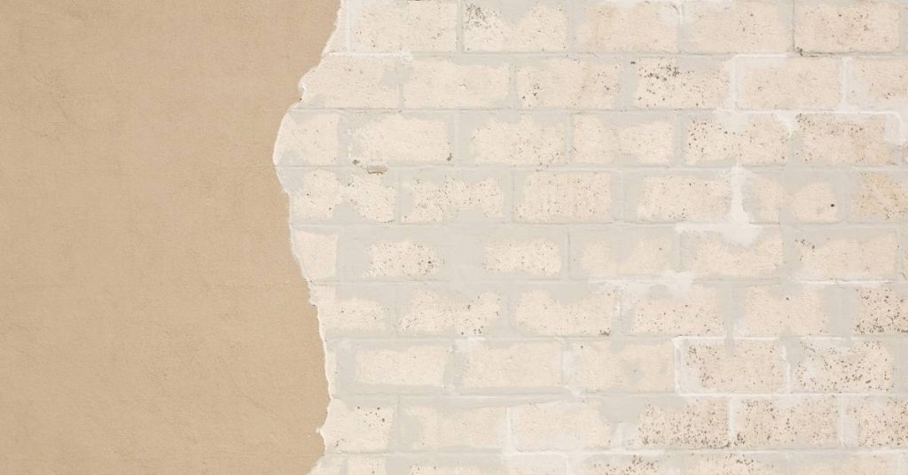 Stucco partially removed revealing underlying brick wall