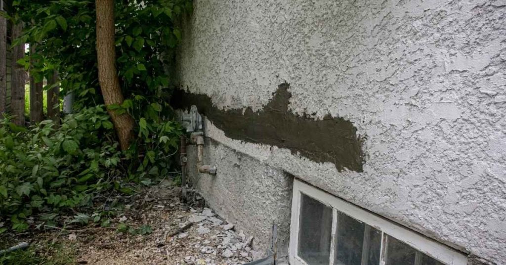 Stucco wall with fresh dark patch repair near window and vegetation