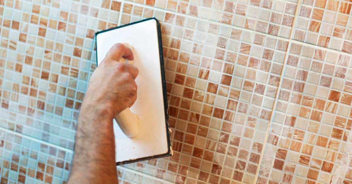 Hand holding grout float applying grout to mosaic tiles