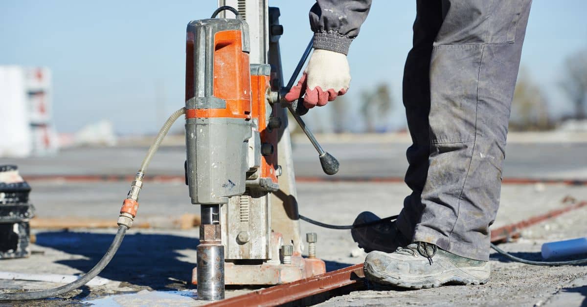 Person operating concrete core drilling machine on construction site