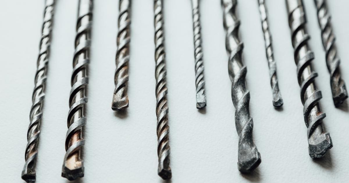 Various sizes of concrete drill bits lined up on a white surface
