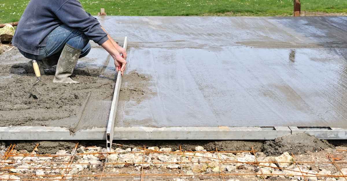 Person leveling wet concrete slab with straightedge tool