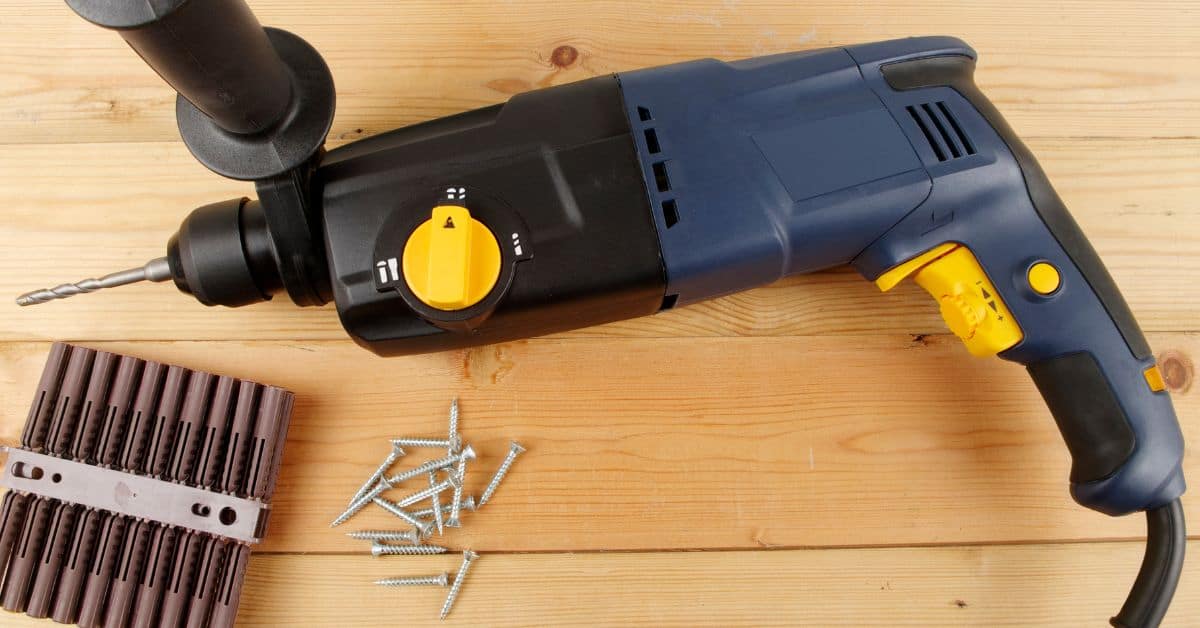 corded hammer drill with screws and wall plugs on wooden surface