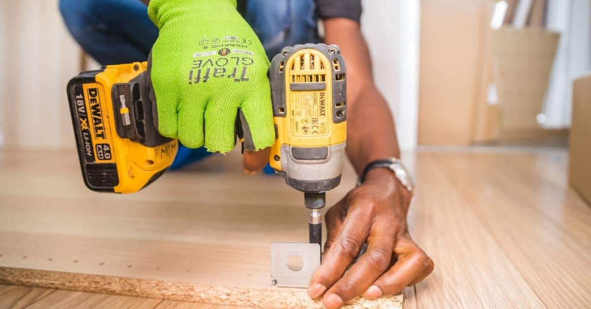 Person using cordless drill on particleboard wearing green glove