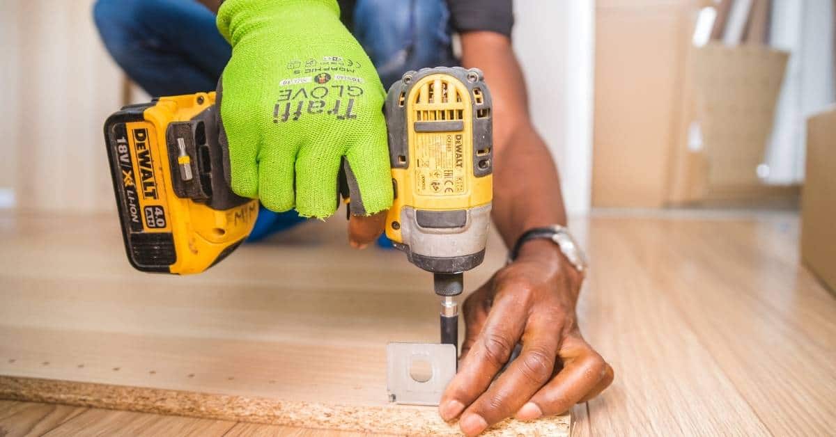 Person wearing green glove using cordless drill on wood