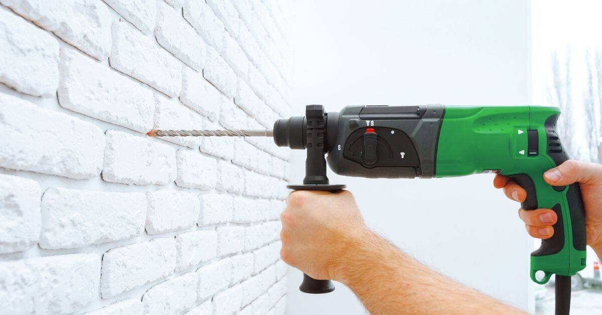 Person using green power drill on white brick wall