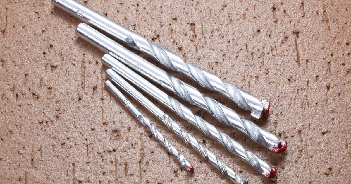 Set of four shiny metal masonry drill bits on brown surface