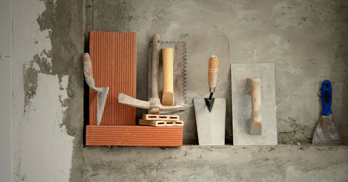 masonry tools including bricks trowels and a hammer on a cement surface