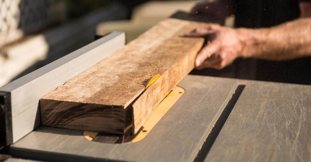 Wood plank being cut on a table saw by hand