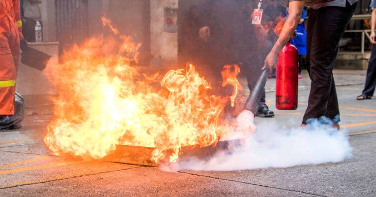 Person using fire extinguisher to put out flames on ground
