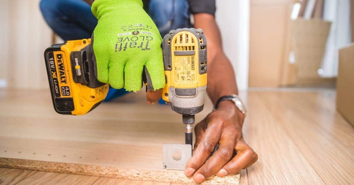 Person using yellow cordless drill on wood with green glove