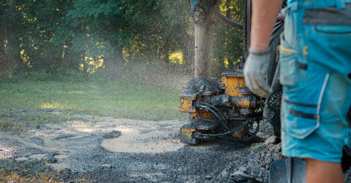 worker operating a yellow drilling machine with soil spraying outdoors