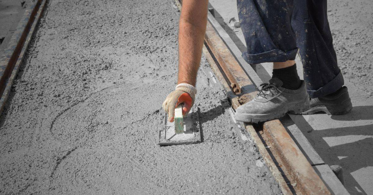 Worker smoothing wet concrete with trowel on construction site