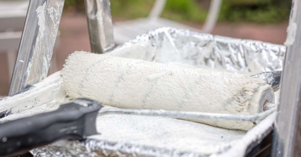 White paint roller resting in paint tray on ladder