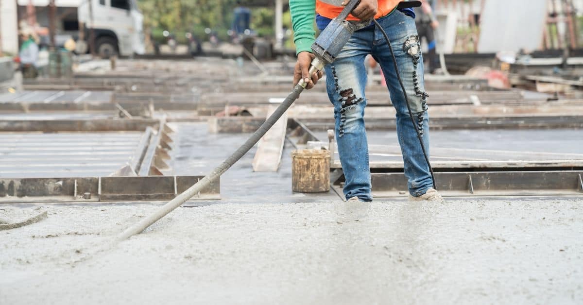 Worker holding concrete hose pouring fresh concrete slab