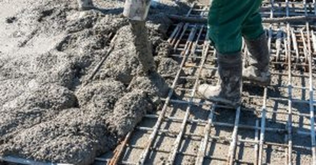 Worker pouring concrete over rebar on construction site