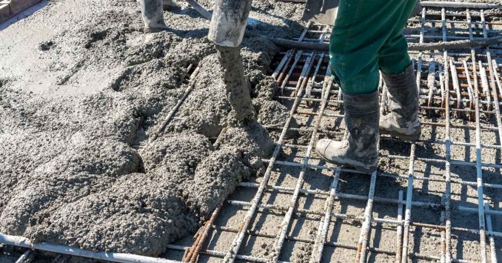 Worker pouring concrete over steel rebar grid
