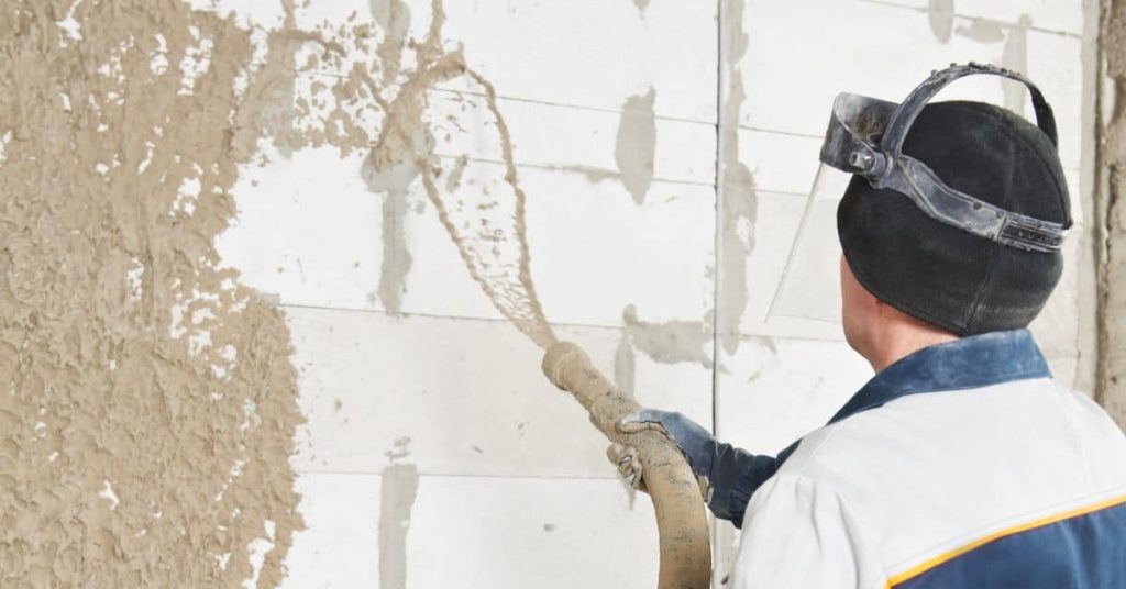 Worker spraying stucco on exterior wall