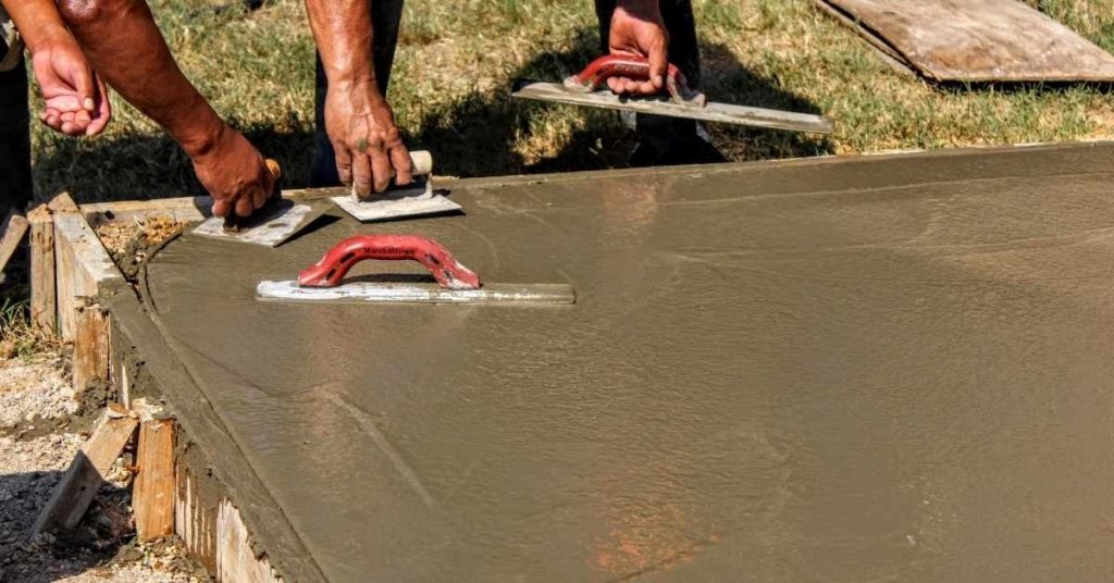 Workers smoothing fresh concrete slab with finishing tools