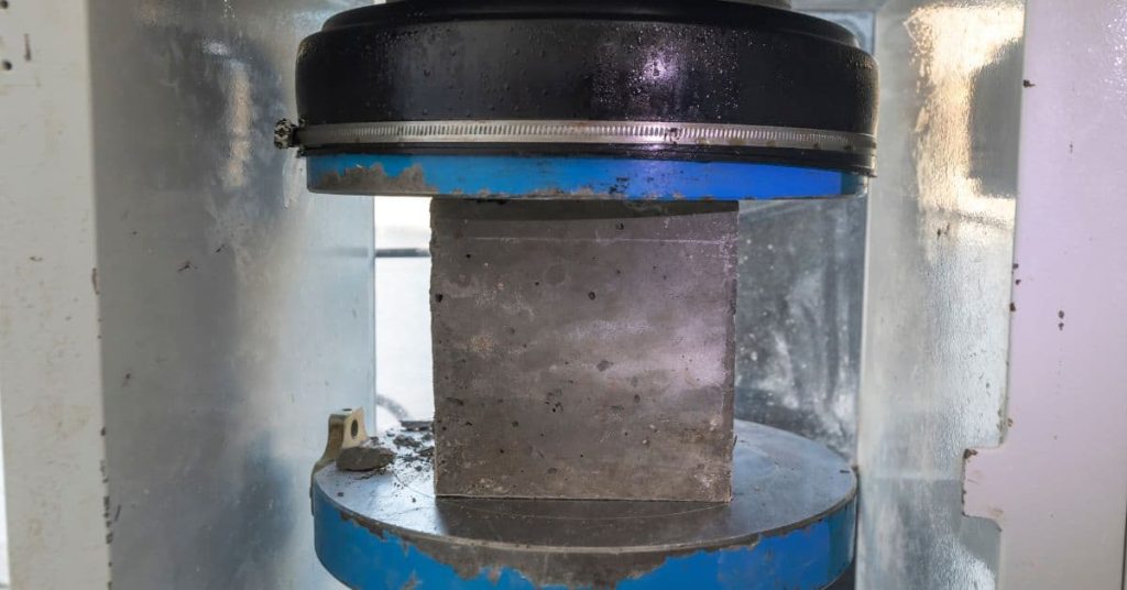 Concrete cube placed in a compression-testing machine for strength testing.
