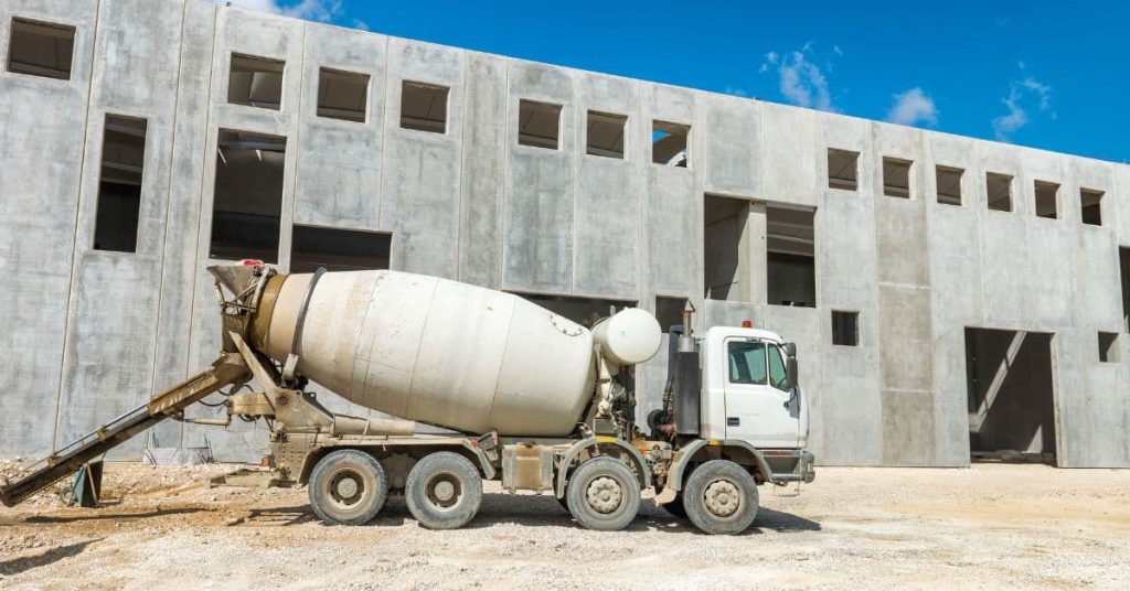 Concrete mixer truck with its discharge chute extended beside an unfinished concrete building