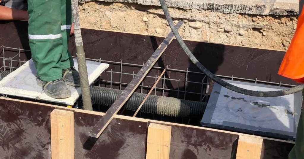 Workers and a concrete hose positioned above reinforcing steel inside concrete formwork