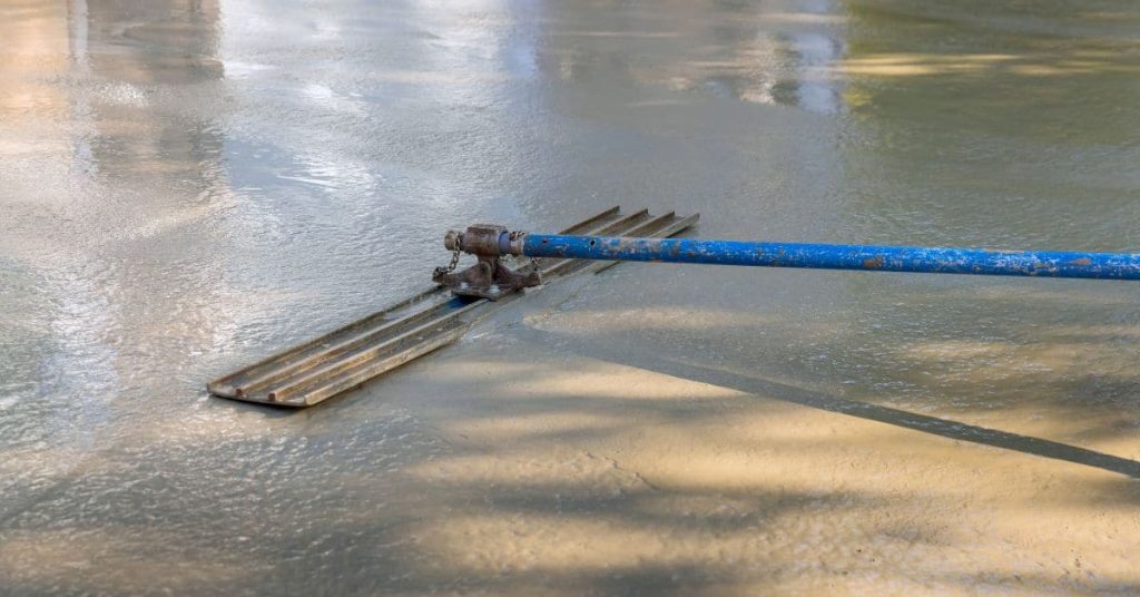 Long-handled finishing tool resting on a wet concrete slab