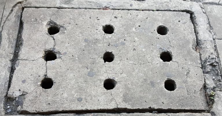 Cracked concrete slab with nine drilled injection holes in a grid pattern and damaged edges