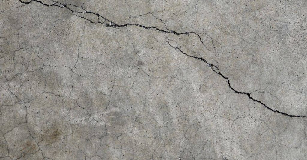 Wide irregular crack with smaller branching cracks across a gray concrete surface