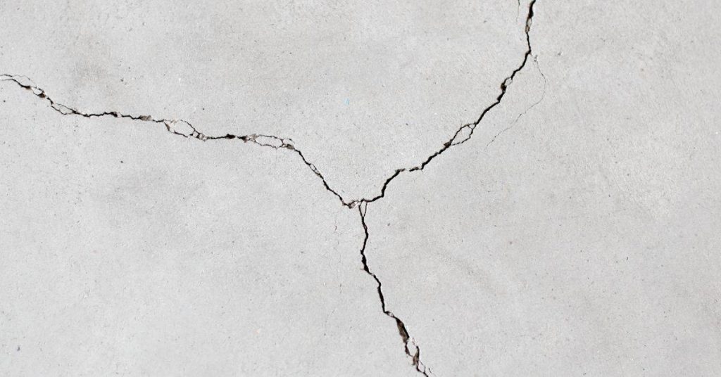 Branching cracks meet at a junction on a light-gray concrete surface.