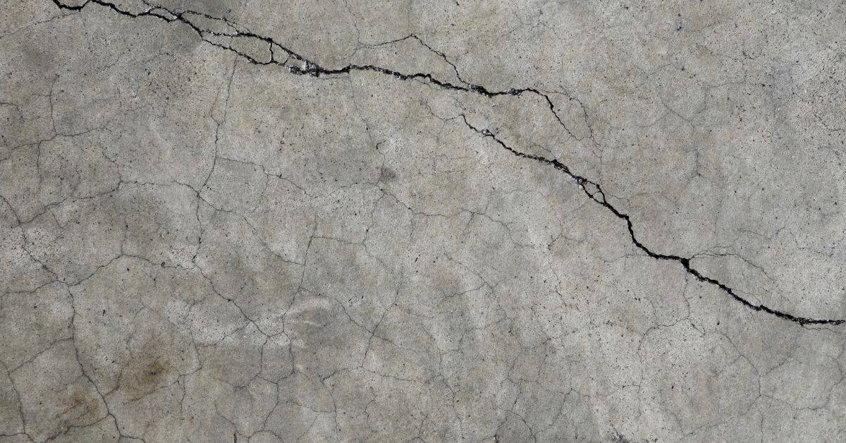 Wide irregular crack with smaller branching cracks across a gray concrete surface
